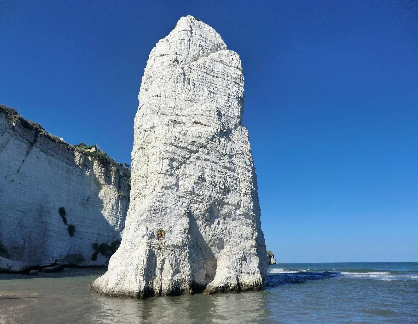 Il monolite bianco del Pizzomunno sulla spiaggia di Vieste, con il centro storico sullo sfondo.